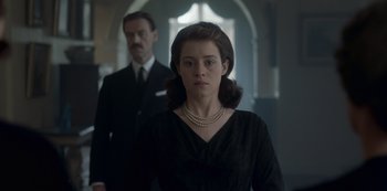Movie still from “The Crown” (2016), created by Peter Morgan – A man and a woman standing in front of each other in a room; Medium shot, Low angle