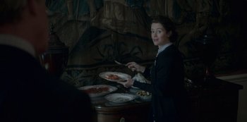 Movie still from “The Crown” (2016), created by Peter Morgan – A woman holding a plate of food in front of plates of pizza; Medium shot, Over the shoulder angle