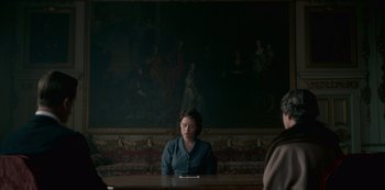 Movie still from “The Crown” (2016), created by Peter Morgan – A woman sitting at a table in front of a painting on the wall; Wide shot, Over the shoulder angle