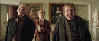 Movie still from “Mr. Turner” (2014), directed by Mike Leigh – A group of men standing next to each other in front of paintings; Medium shot, Low angle