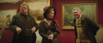 Movie still from “Mr. Turner” (2014), directed by Mike Leigh – A woman wearing a hat standing in front of a painting; Medium shot, Low angle