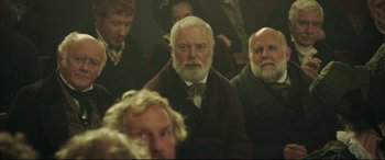 Movie still from “Mr. Turner” (2014), directed by Mike Leigh – A group of men sitting in a room; Medium shot, Over the shoulder angle