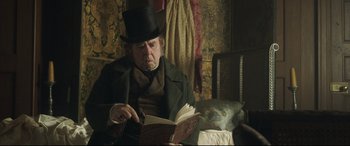 Movie still from “Mr. Turner” (2014), directed by Mike Leigh – An older man in a top hat and coat reading a book; Medium shot, Over the shoulder angle