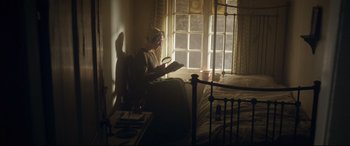 Movie still from “Mr. Turner” (2014), directed by Mike Leigh – A woman sitting in a chair reading a book in a dimly - lit room; Wide shot, High angle