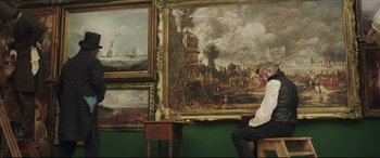 Movie still from “Mr. Turner” (2014), directed by Mike Leigh – A man sitting in front of two paintings; Wide shot, Over the shoulder angle