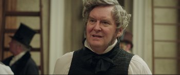Movie still from “Mr. Turner” (2014), directed by Mike Leigh – An older man wearing a black vest and a bow tie; Close Up shot, Over the shoulder angle