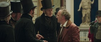 Movie still from “Mr. Turner” (2014), directed by Mike Leigh – A group of men standing next to each other in a room; Medium shot, Over the shoulder angle
