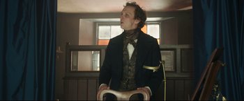 Movie still from “Mr. Turner” (2014), directed by Mike Leigh – A man in a suit and tie sitting in a room; Medium shot, Low angle