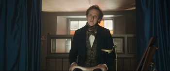 Movie still from “Mr. Turner” (2014), directed by Mike Leigh – A man in a suit and bow tie sitting in a chair; Medium shot, Low angle