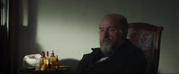 Movie still from “Mr. Turner” (2014), directed by Mike Leigh – An older man sitting in front of some bottles; Medium shot, Over the shoulder angle