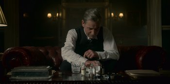 Movie still from “The Crown” (2016), created by Peter Morgan – An older man sitting at a table in front of a bottle; Medium shot, Low angle
