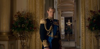 Movie still from “The Crown” (2016), created by Peter Morgan – A man in a military uniform standing in a room; Medium shot, Low angle