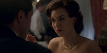 Movie still from “The Crown” (2016), created by Peter Morgan – A woman with a gold chain around her neck; Close Up shot, Over the shoulder angle