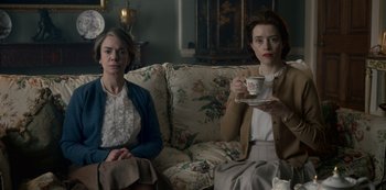 Movie still from “The Crown” (2016), created by Peter Morgan – Two women are sitting on a couch and drinking tea; Medium shot, Low angle