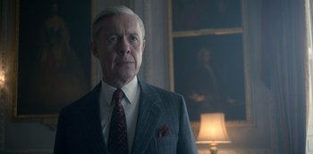 Movie still from “The Crown” (2016), created by Peter Morgan – An older man wearing a suit and tie in front of a lamp; Close Up shot, Over the shoulder angle