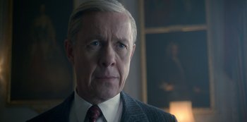 Movie still from “The Crown” (2016), created by Peter Morgan – An older man in a suit and tie looking at the camera; Close Up shot, Over the shoulder angle
