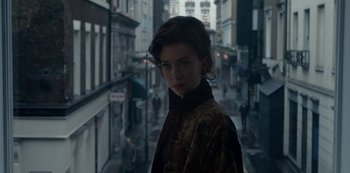 Movie still from “The Crown” (2016), created by Peter Morgan – A woman in a brown coat standing on a city street; Close Up shot, Low angle