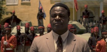 Movie still from “The Crown” (2016), created by Peter Morgan – A man wearing a suit and tie standing in front of a group of men; Close Up shot, Low angle