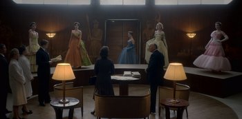 Movie still from “The Crown” (2016), created by Peter Morgan – A group of people standing in front of a mirror in a room; Wide shot, Low angle
