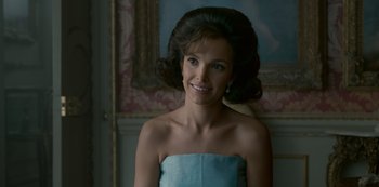 Movie still from “The Crown” (2016), created by Peter Morgan – A woman in a strapless blue dress smiling for the camera; Close Up shot, Over the shoulder angle