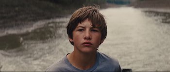 Movie still from “Mud” (2012), directed by Jeff Nichols – A young man in a blue shirt is by the water; Close Up shot, Low angle