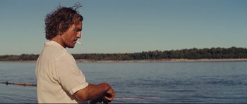Movie still from “Mud” (2012), directed by Jeff Nichols – A man is smoking a cigarette while fishing on a lake; Medium shot, Over the shoulder angle