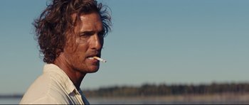 Movie still from “Mud” (2012), directed by Jeff Nichols – A person smoking a cigarette near a body of water; Close Up shot, Over the shoulder angle