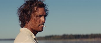 Movie still from “Mud” (2012), directed by Jeff Nichols – A person smoking a cigarette near a body of water; Close Up shot, Over the shoulder angle