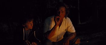 Movie still from “Mud” (2012), directed by Jeff Nichols – A man sitting next to another man smoking a cigarette in the dark; Medium shot, Over the shoulder angle