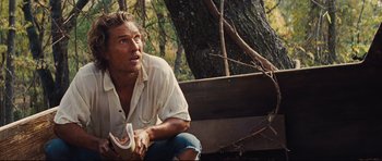 Movie still from “Mud” (2012), directed by Jeff Nichols – A man sitting on the ground near a tree; Medium shot, Low angle