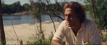 Movie still from “Mud” (2012), directed by Jeff Nichols – A person sitting on the ground near a body of water; Close Up shot, Over the shoulder angle