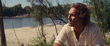 Movie still from “Mud” (2012), directed by Jeff Nichols – A person sitting on a bench near a body of water; Close Up shot, Over the shoulder angle