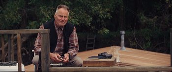 Movie still from “Mud” (2012), directed by Jeff Nichols – An older man sitting on the ground next to a pair of binoculars; Medium shot, Over the shoulder angle