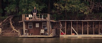 Movie still from “Mud” (2012), directed by Jeff Nichols – A man sitting on top of a wooden house on a river; Extreme Wide shot, Low angle