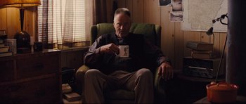 Movie still from “Mud” (2012), directed by Jeff Nichols – An older man sitting in a chair holding a cup; Medium shot, Over the shoulder angle