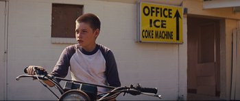 Movie still from “Mud” (2012), directed by Jeff Nichols – A young boy sitting on a bike in front of a building; Medium shot, Low angle