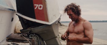 Movie still from “Mud” (2012), directed by Jeff Nichols – A shirtless man standing next to an old boat; Medium shot, Low angle