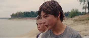 Movie still from “Mud” (2012), directed by Jeff Nichols – Two young boys standing next to each other near a body of water; Close Up shot, Over the shoulder angle