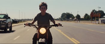 Movie still from “Mud” (2012), directed by Jeff Nichols – A man riding a motorcycle down the middle of the road; Medium shot, Low angle