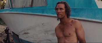 Movie still from “Mud” (2012), directed by Jeff Nichols – A man with long curly hair and no shirt is standing in front of a wall; Close Up shot, Low angle