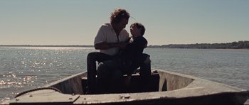Movie still from “Mud” (2012), directed by Jeff Nichols – A man and a boy sitting on a boat in the water; Medium shot, Low angle