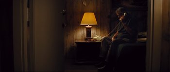 Movie still from “Mud” (2012), directed by Jeff Nichols – A man sitting on a chair in front of a lamp; Wide shot, High angle
