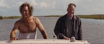 Movie still from “Mud” (2012), directed by Jeff Nichols – A man sitting on the back of a boat next to another man; Medium shot, Low angle