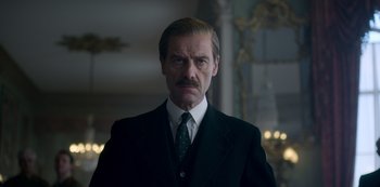 Movie still from “The Crown” (2016), created by Peter Morgan – A person wearing a suit and tie; Close Up shot, Low angle