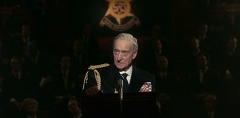 Movie still from “The Crown” (2016), created by Peter Morgan – An older man in a military uniform is speaking; Medium shot, Low angle