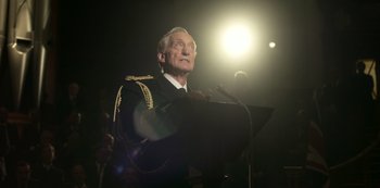 Movie still from “The Crown” (2016), created by Peter Morgan – An older man in a military uniform speaking at a podium; Close Up shot, Low angle