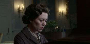 Movie still from “The Crown” (2016), created by Peter Morgan – An older woman in a brown suit looking down at her face; Close Up shot, Low angle