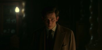 Movie still from “The Crown” (2016), created by Peter Morgan – A man wearing a suit and tie standing in the dark; Close Up shot, Low angle
