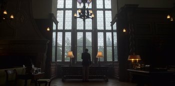 Movie still from “The Crown” (2016), created by Peter Morgan – A man standing in front of a large window; Wide shot, Low angle