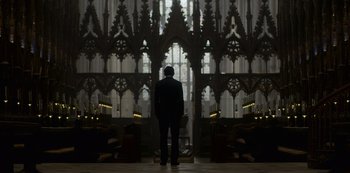Movie still from “The Crown” (2016), created by Peter Morgan – A man standing in front of an altar in a church; Extreme Wide shot, Low angle